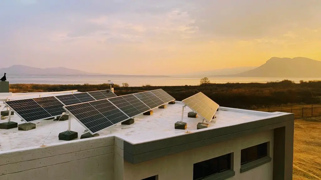 Panels on a flat roof at sunset, with the Magaliesberg behind